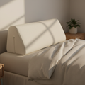 Cream-colored memory foam wedge pillow with soft removable cover on a neatly made bed with sand linen sheets